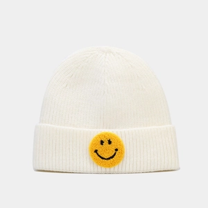 Détail du tricot du bonnet blanc cassé avec écusson smiley jaune sur le bord replié