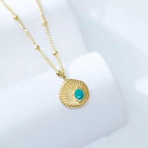 Macro shot of gold sunburst pendant with a turquoise center stone on a minimalist stand