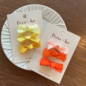 Detailed view of colorful grosgrain ribbon hair bows on a card over a textured tray