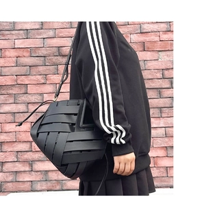 Detail of black woven leather bucket bag with geometric design worn over the shoulder