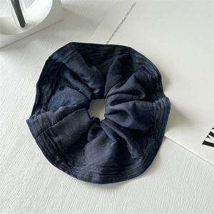 Detailed view of deep blue denim fabric scrunchie on a clean white textured surface