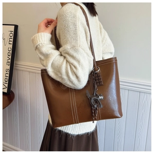 Brown tote bag with white stitching detail and a cute cat charm on casual shoulder strap