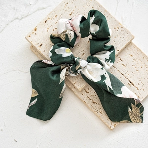 Detailed view of dark green floral satin scrunchie with long ribbon on beige stone slabs