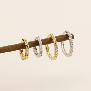 Détail de quatre créoles en or et argent avec de petits zircons sur une tige en bois