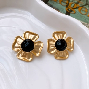 Detailed view of vintage gold flower stud earrings with black center on a ceramic plate