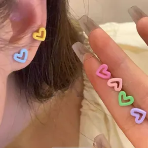 Close-up of matte heart-shaped stud earrings in candy colors set on ears and fingers