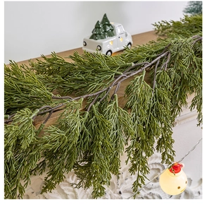 Detail of lush green PE cypress garland draped on a wooden mantelpiece with warm lights