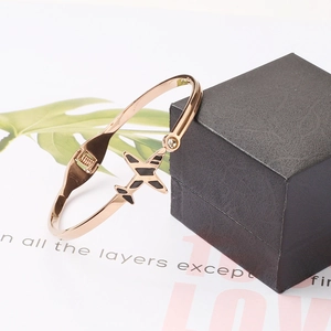 Détail d'un bracelet avion en or rose avec émail noir posé sur un coffret à bijoux