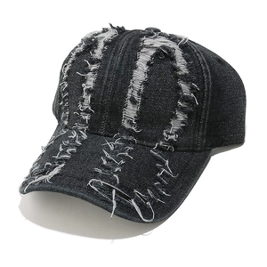 Detailed view of frayed holes and metal safety pin on washed black denim baseball cap