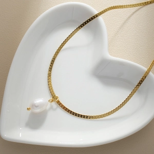Layered gold snake chain necklace with irregular freshwater pearl pendant on ceramic tray