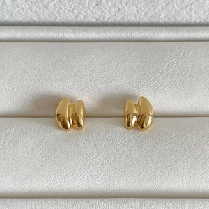 Polished gold geometric stud earrings displayed in a white textured jewelry box