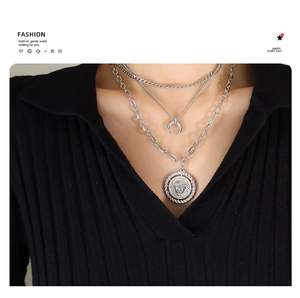 Detail of triple-layer silver necklace with crescent and lion head medallion charms