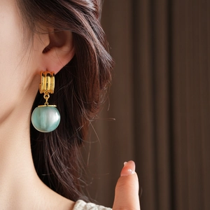Close-up of elegant gold hoop earrings with translucent green resin sphere pendants