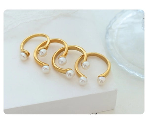 Detail of four gold U-shaped rings with baroque pearls arranged on a white stand