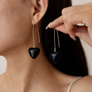Close-up of elegant black heart drop earrings with long gold chains worn by a model