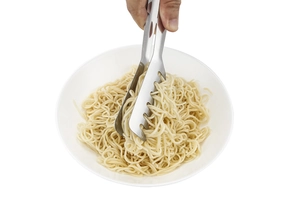 Macro shot of stainless steel food tongs picking up spaghetti from a white plate