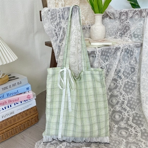 Detailed close-up of a green plaid tote bag with delicate lace bow on a wooden chair