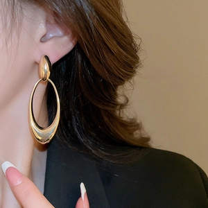 Macro detail of large gold oval hoop earrings with shiny metallic finish on model
