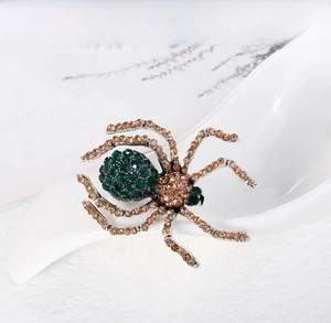 Detailed close-up of a spider brooch with green and brown rhinestones in a ceramic spoon