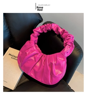 Detail of rose red ruched hobo bag with cloud pleats on black leather surface