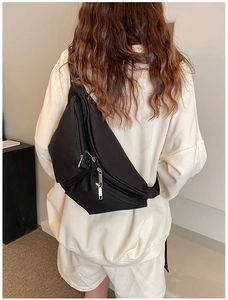 Detail of black crossbody bag with dual zippers and adjustable wide shoulder strap on model