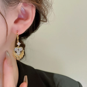 Close-up of gold heart earrings with white zircons and tassels worn by a female model