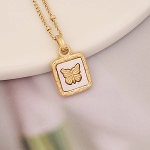 Close-up of golden butterfly pendant necklace with textured shell inlay on white tray