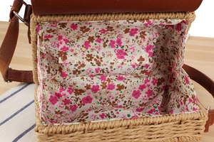 Detail view of woven paper rope bag featuring floral fabric lining and brown leather flap