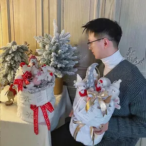 Seau cadeau bouquet de Noël avec poupées en peluche et rubans festifs tenu à la main