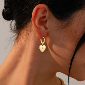 Detail of 18K gold heart earrings with sparkling starburst centered gemstone inlay