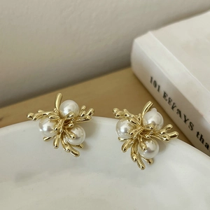 Detailed view of 18k gold-plated pearl branch earrings on a white porcelain bowl edge