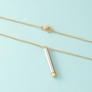 Polished gold and silver cylinder pendant necklace on light blue background
