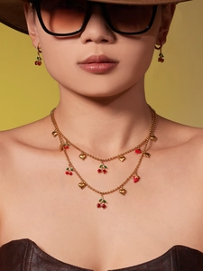 Gros plan d'un mannequin portant une parure de bijoux cerise avec chaîne dorée double
