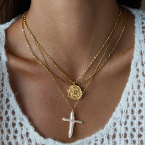 Detail of layered gold necklaces with a coin pendant and a baroque pearl cross pendant