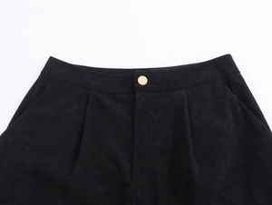 Dettaglio del bottone dorato e della vita a pieghe su pantaloncini di velluto nero