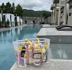 Transparent mesh beach tote with pink handles at poolside, showing ample storage space