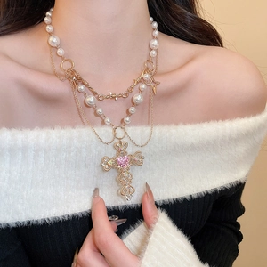 Detail of layered pearl necklace featuring cross pendant and pink heart gemstone