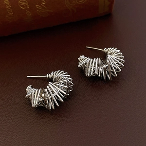 Detailed shot of silver C-shaped multi-layer twisted metal earrings on a leather surface