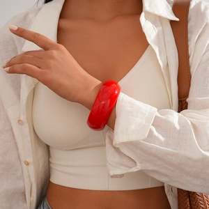 Close-up of a wide red acrylic resin bangle on a model's wrist with polished finish