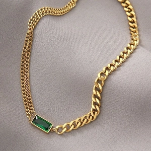 Close-up of gold double-layer chain with emerald zircon pendant on gray fabric