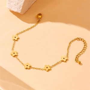 Elegant gold flower chain bracelet with five floral charms on a textured stone background