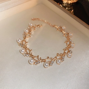 Macro view of gold chain bracelet with pearl accents and rhinestone leaf charms in a gift box