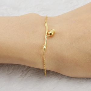 Minimalist 18K gold rose flower branch bracelet on female wrist with white fur background