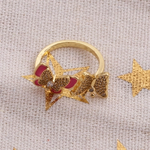 Detail of gold butterfly ring with pink glaze and white zircons on beige fabric