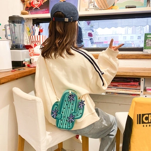 Trendy cactus-shaped green crossbody bag with gold chain strap shown on a model in a cafe