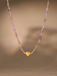 Detail of beaded necklace with purple stones, gold beads, and a heart pendant charm