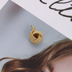 Detailed view of an 18K gold braided knot charm placed on a fashion magazine page