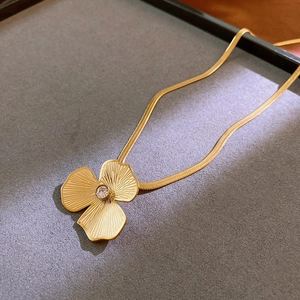 Close-up of golden clover pendant necklace with centered crystal on velvet tray