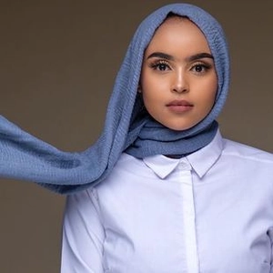 Detalle de textura arrugada en un hiyab de algodón azul grisáceo con camisa blanca