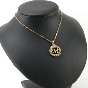 Collier lettre M en acier inoxydable plaqué or 18K avec cristaux sur support noir élégant